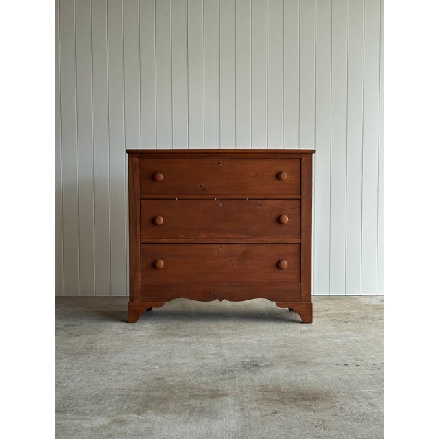 Antique pine chest of drawers with a scalloped apron and original turned wooden knobs, the surface showing soft, sun-...