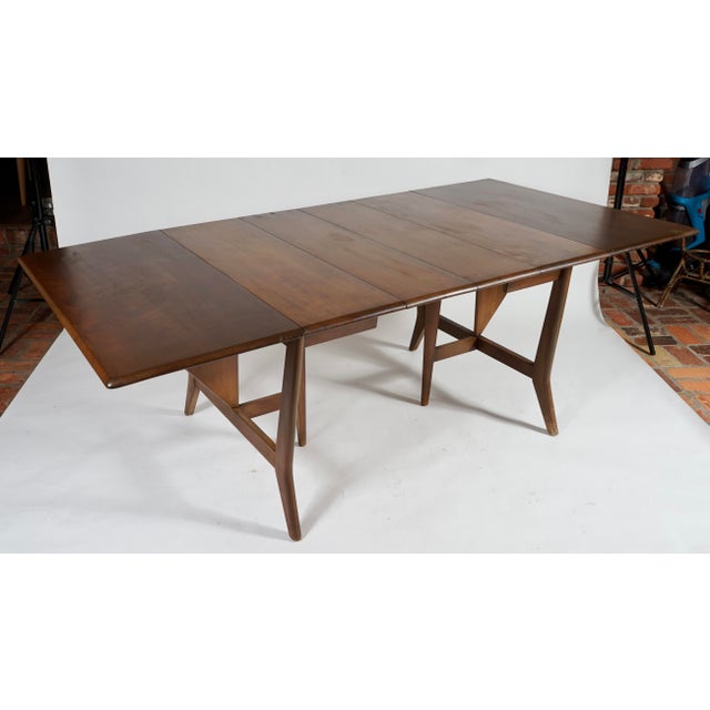 This Heywood Wakefield mid-century maple dining table features a distinct drop-leaf design with a rich brown finish. A mid...