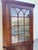 Beautiful antique wood corner cabinet featuring a wavy glass-paneled upper display with Gothic arch mullions, decorative...