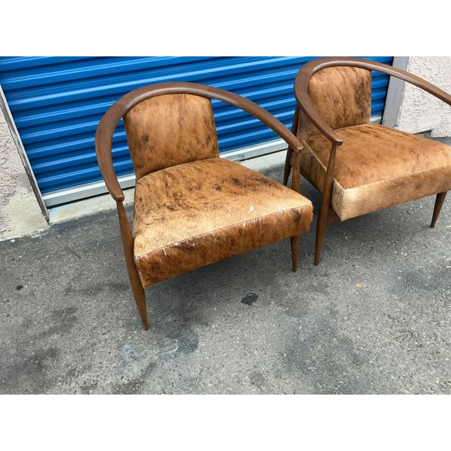 Modern mid century lounge chairs done in a multi colored brown cowhide upholstery. The chairs have a walnut finish. The...