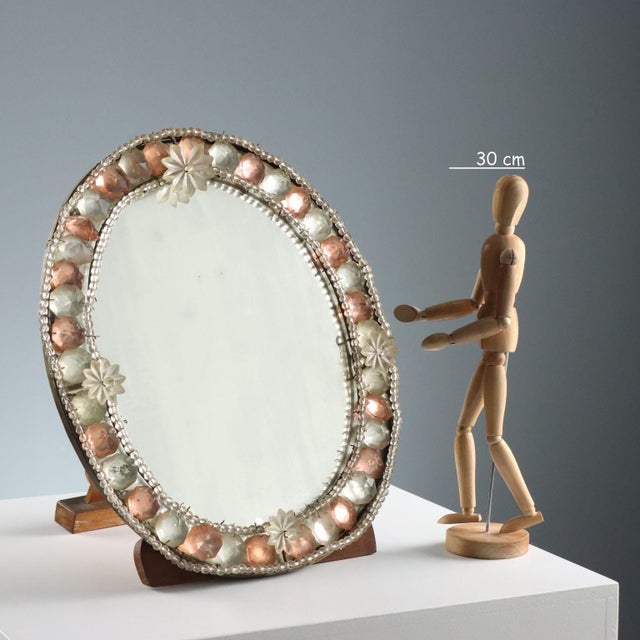 Table mirror with beaded frame, gems, and clear and pink glass flowers. Wooden frame. This piece is attributed to the...