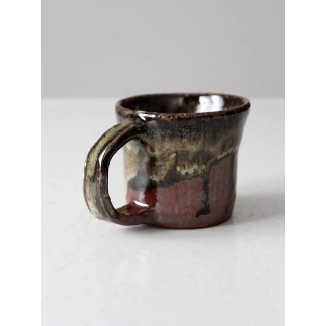 This vintage studio pottery mug is a genuine hand-thrown ceramic piece with rich earth tone glazes in deep browns, creams,...
