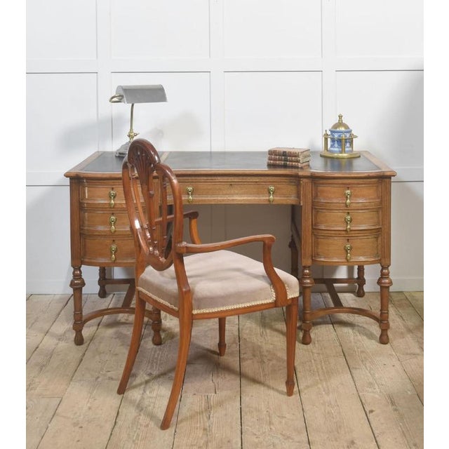 Constructed in well-figured oak with a warm, even patina, the desk features a gently serpentine front and a tripartite...