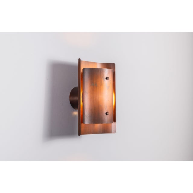 This vintage Danish wall lamp is distinguished by its sculptural composition of two opposing, shield-like copper elements...