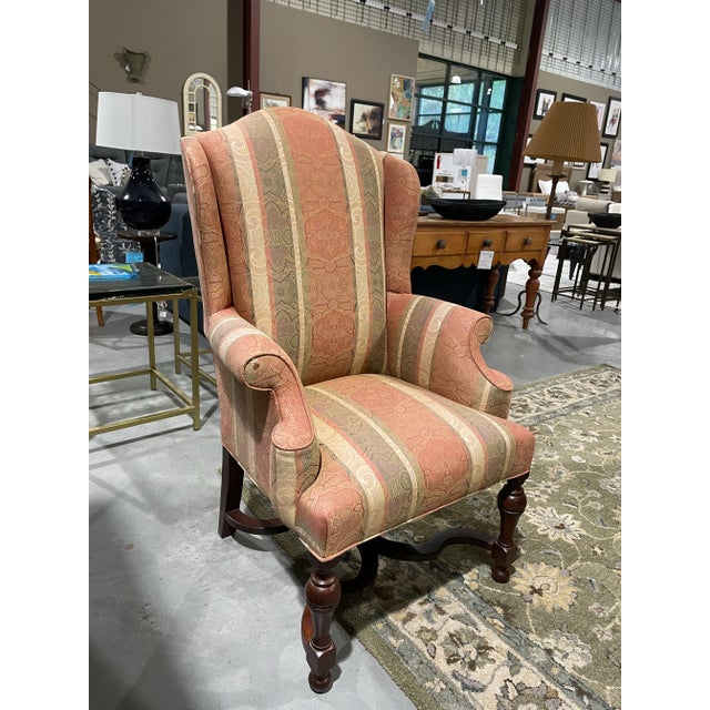 This classic wingback armchair showcases timeless elegance with its high back, rolled arms, and finely carved wooden legs....