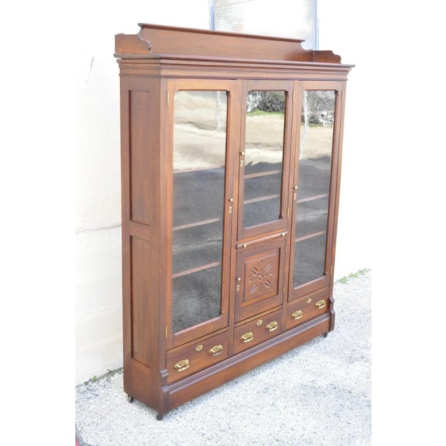 Antique Eastlake Victorian Walnut Wavy Glass Triple Bookcase Display Cabinet. Item features 16 adjustable wooden shelves...