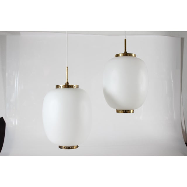 Set of two large China pendents made of off-white opaline glass and with brass fittings. The pendants are designed by...
