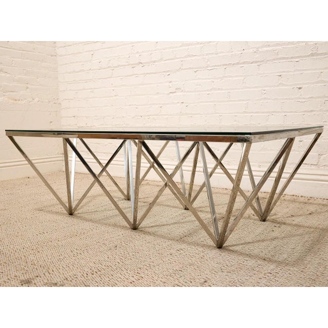 A striking modern coffee table with a sculptural chrome base built from intersecting angular supports. The geometric...