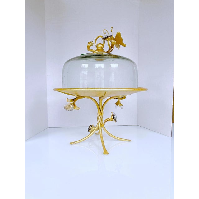 This is decorative Iron cake stand with hand blown glass dome. The iron stand is painted in gold finish and decorated with...