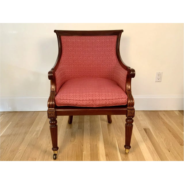 A vintage regency style armchair upholstered in a textured, raspberry fabric with a geometric pattern, a slightly scrolled...