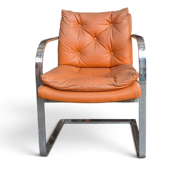 A vintage cantilever lounge chair with a continuous chrome-finish steel frame and tufted orange vinyl upholstery. The open...
