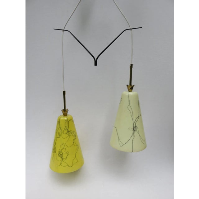 This 1950s pendant features two fiberglass shades in yellow and beige with black strings fixed to a black lacquered brass...