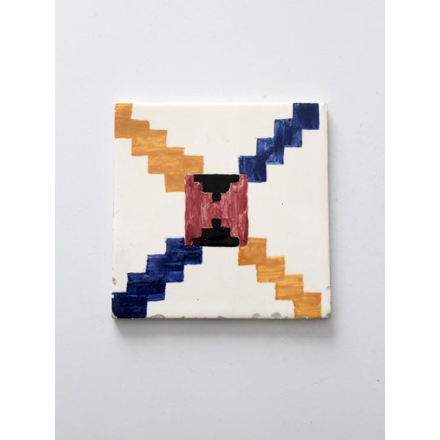A mid-20th century hand-painted ceramic tile with a bold geometric, textile-inspired design in deep blue, mustard, brick...