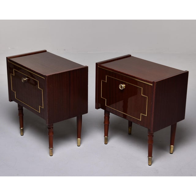 This pair of Mid-Century nightstands features drop-front doors with brass geometric inlay forming stepped corner motifs....