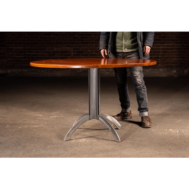 Round hardwood café or dining table featuring a thick, solid-wood top with a warm, medium-brown finish set over a welded...