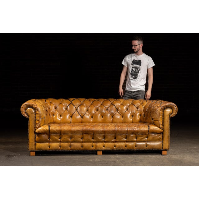 Tufted leather Chesterfield sofa featuring a fully upholstered back and rolled arms of equal height. This classic English...