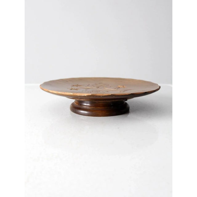 This is a vintage wooden cake stand featuring a pedestal base and a finely carved floral design across the surface of the...