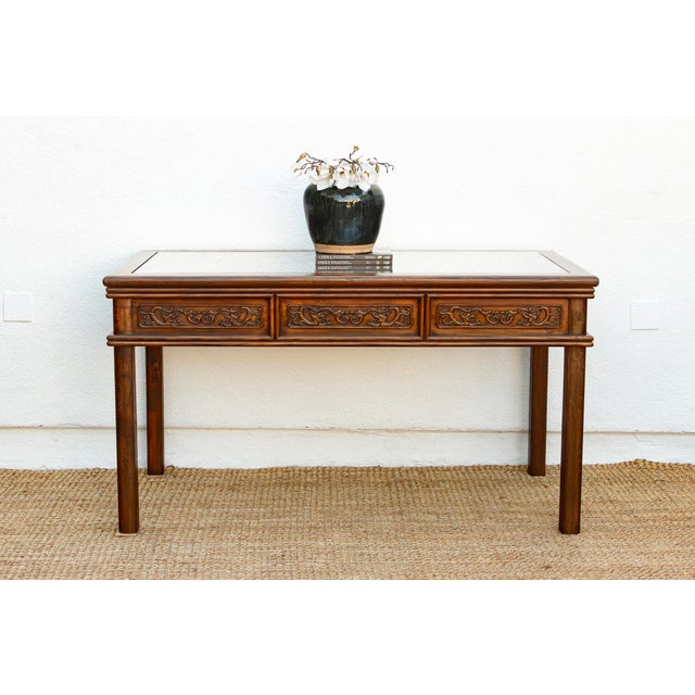 A long Chinese center table in dark walnut-brown wood, built to be seen from every side. A carved lattice panel sits...