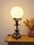 This elegant lamp combines a white opaline glass shade with a richly crafted wrought iron frame, evoking the aesthetics of...