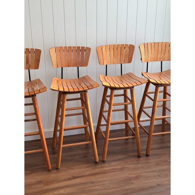 A set of four mid-century modern bar stools with slatted backs, sculpted seats, and swivel bases, constructed from solid...