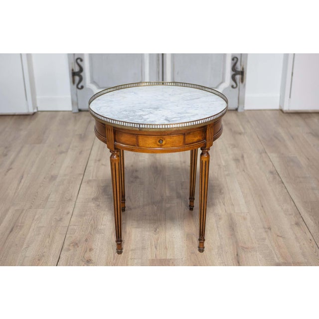 A French Louis XVI style walnut bouillotte table from the 20th century with white and gray variegated marble top, pierced...
