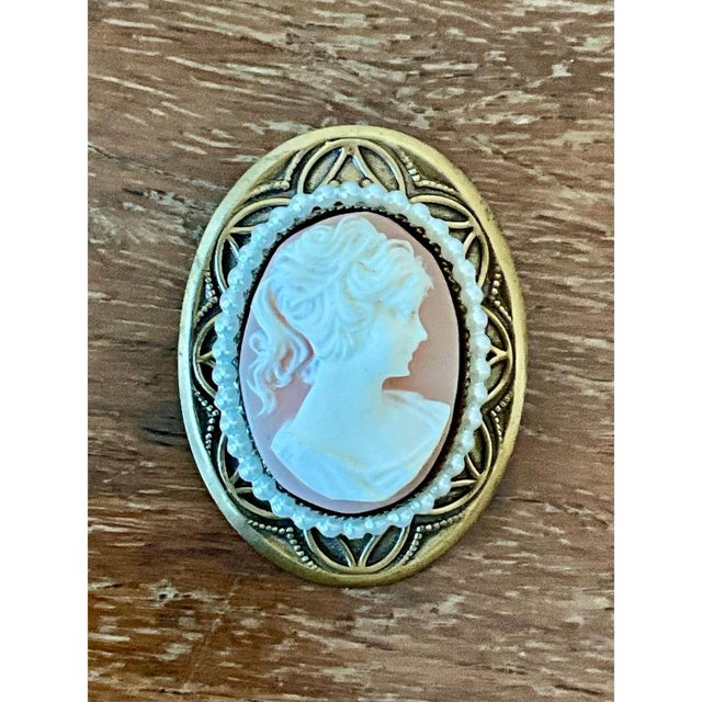 This vintage gold-tone cameo pendant brooch showcases a softly romantic female profile, her wavy hair cascading loosely...