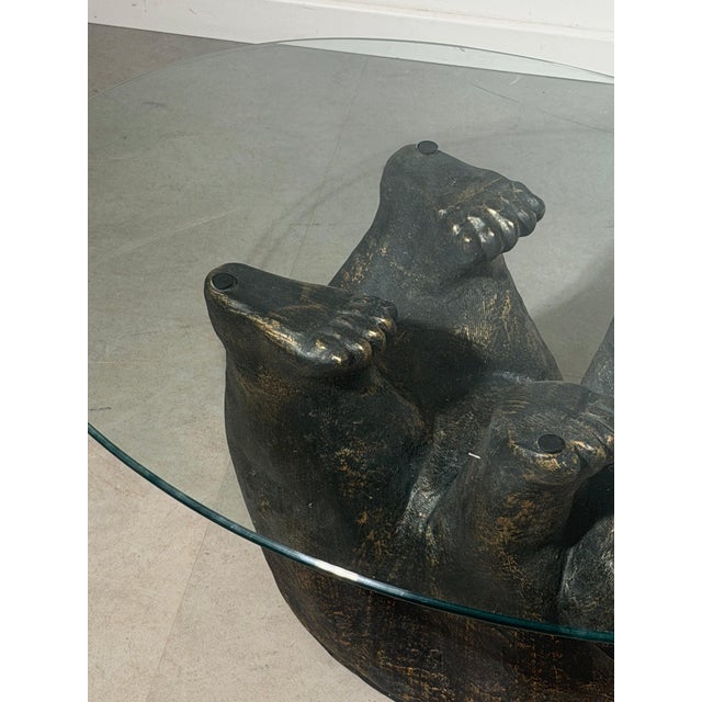 Unique and eye-catching coffee table featuring a sculptural black bear in resin, playfully supporting an oval glass top....