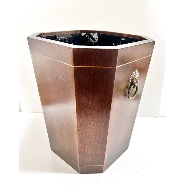 A handsome vintage wood wastebasket with a rich mahogany-tone finish, brass-tone banding, and classical lion head ring...