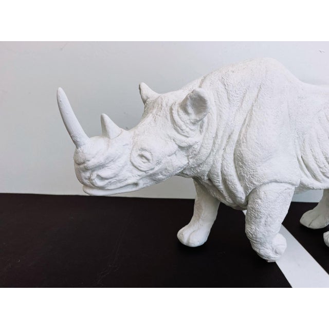 Large plaster sculpture of a white rhinoceros in walking pose with lifelike incised detailing in a matte white finish....