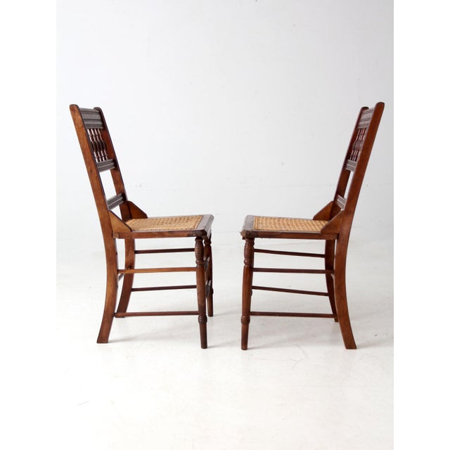 A late 19th century pair of American Eastlake side chairs with turned spindle backs and woven cane seats. The vertical...