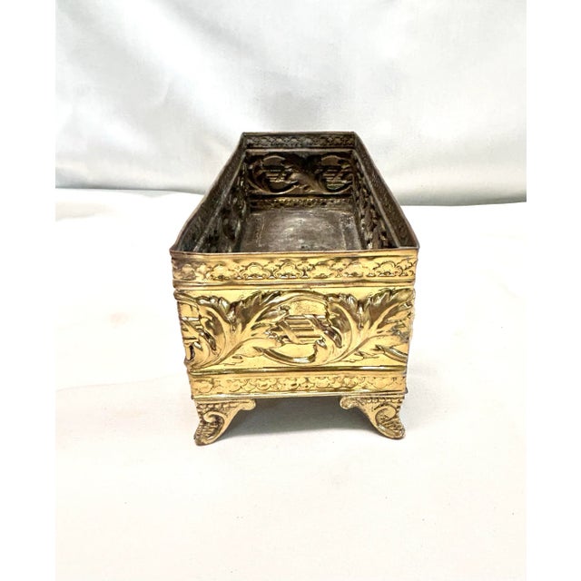 A beautifully detailed brass cachepot featuring embossed floral motifs that wrap around the vessel and delicate raised...
