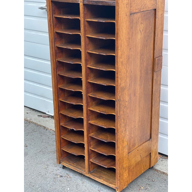 A vintage oak storage accessory cabinet featuring a tall, narrow profile with fixed shelves and dual compartments.Designed...