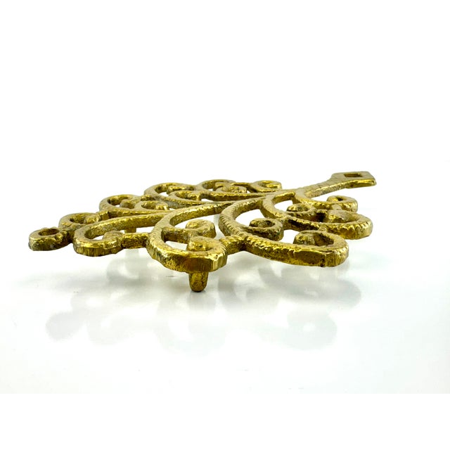 This vintage cast brass trivet features an ornate tree motif formed by scrolling branches and symmetrical openwork...
