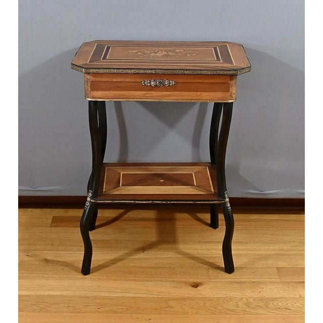 This walnut and rosewood worker, inlaid with light wood, in the Napoleon III style, has a canted top surrounded by an...