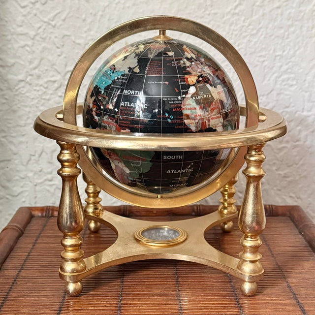 A fine black globe inlaid with semiprecious gemstones; including mother of pearl, amethyst, african jade, tiger's eye,...
