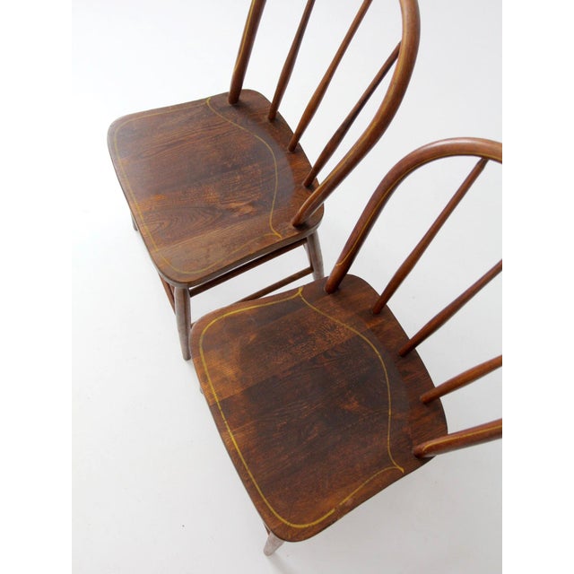 A charming pair of vintage Square Brand Windsor dining chairs featuring classic bow back silhouettes, sculpted wood seats,...
