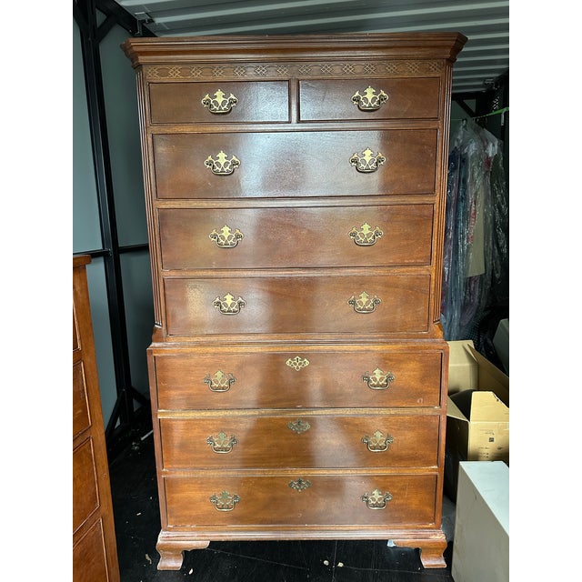 Traditional Colonial Revival Chippendale-style mahogany-finish highboy/chest-on-chest featuring a molded cornice, carved...