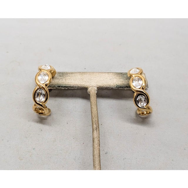 1989 goldtone looped design with oval clear rhinestones pierced push back hoop earrings. Marked "NAPIER©" on the backs....