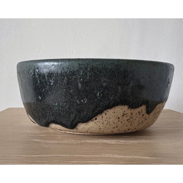 American studio pottery bowl with a low cylindrical profile and dramatic black glaze flowing irregularly over a warm,...