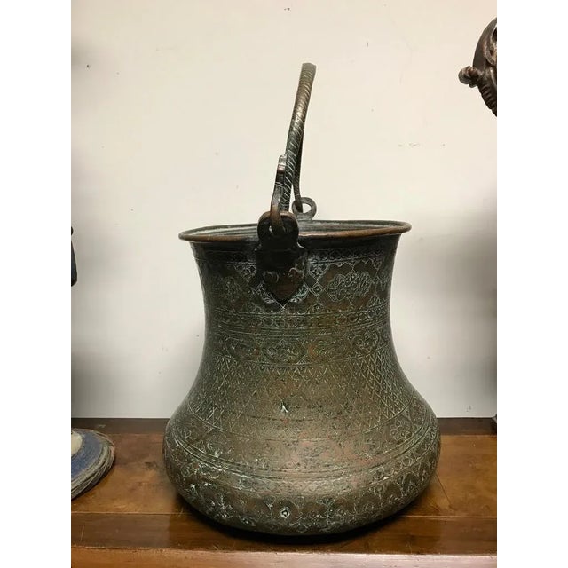 A large scale 17th century Persian etched copper bucket of waisted form on a short foot with hinged handle, profusely...