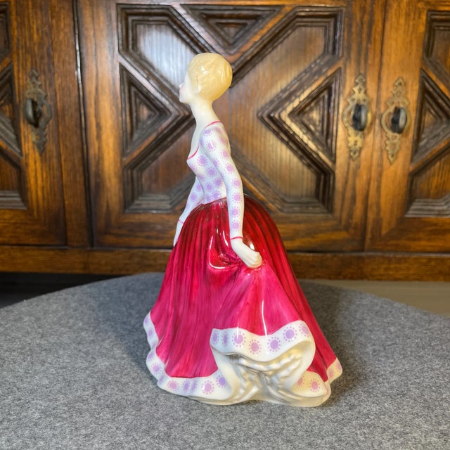 A figure of a young lady in a magenta skirt and pink floral top. Royal Doulton backstamp.