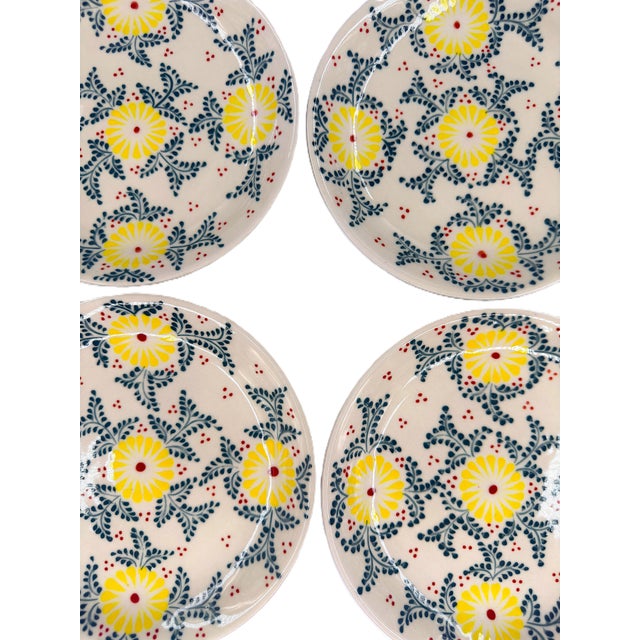 A cheerful set of four Bat Trang ceramic dessert plates featuring a delicate floral design in sunny yellow, deep blue, and...