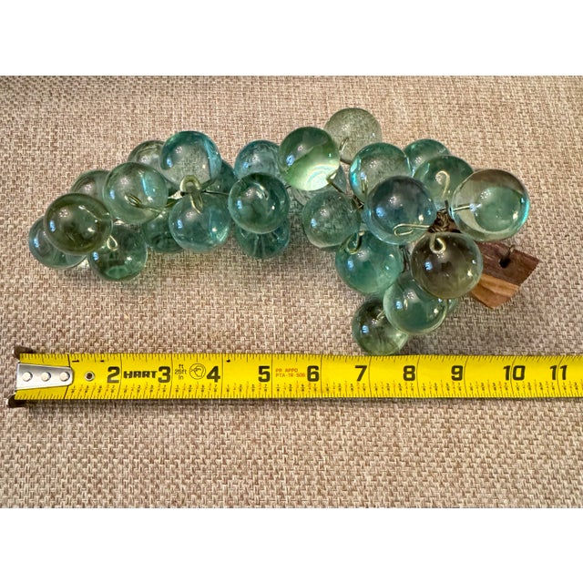 This vintage mid-century decorative grape cluster features translucent aqua Lucite grapes hand-wired to a carved natural...