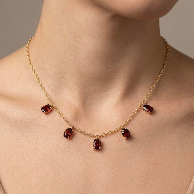 Refined and effortlessly elegant, this Garnet Dangle Station Necklace features five vibrant oval-cut garnet gemstones...