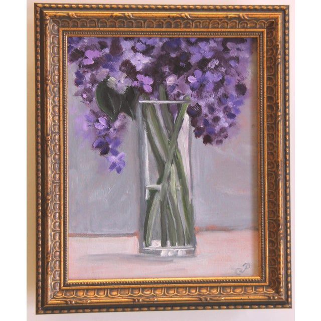 An oil painting of a vase of Lilacs painted in a textured impressionist style on a gray interior background, and framed in...
