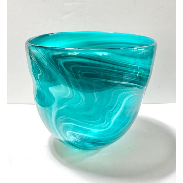 A striking hand-blown art glass vessel featuring dramatic turquoise and aqua swirled striations. The sculptural organic...