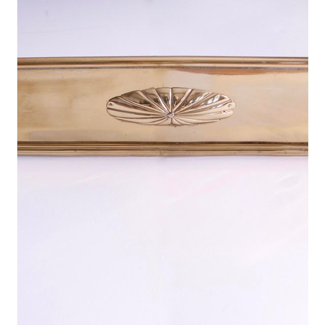 A sleek solid brass English panel fireplace fender centered on a high relief embossed oval brass patera and with...