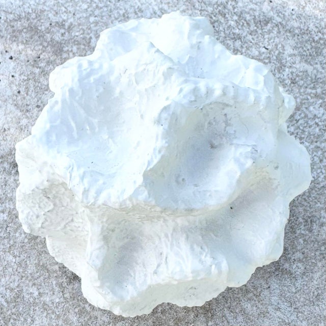 A sculptural minimalist abstract object featuring an irregular spherical form with deeply textured, organic contours. The...