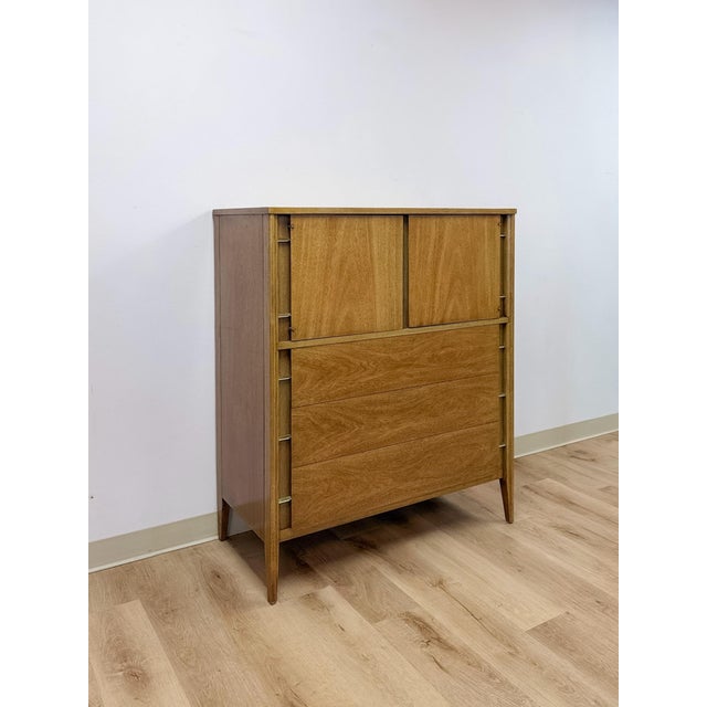 This clean and well-proportioned vintage mid-century modern tallboy dresser with brass accents is a classic and versatile...