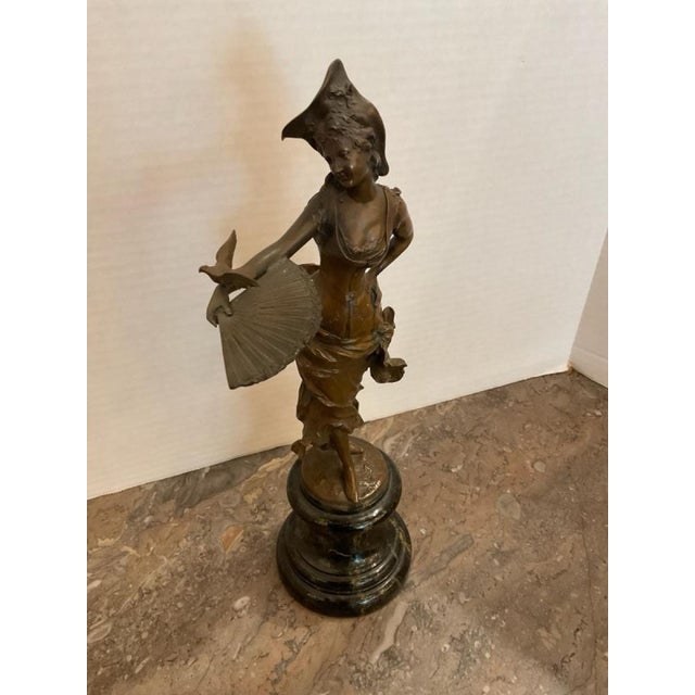 This listing features a bronze patinated cast sculpture of a female figure dressed in Rococo-style attire with a...